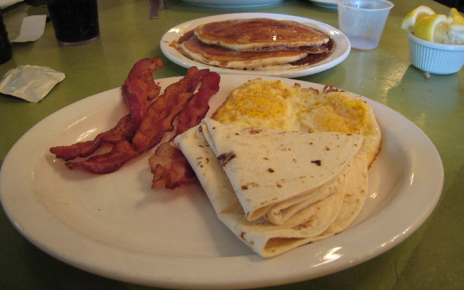 Two eggs, three pieces of bacon and a short stack with a tortilla