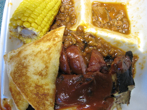 A combo platter with baked beans and corn on the cob